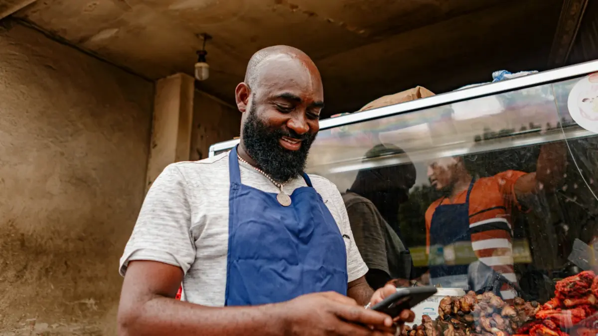 A market trader in an apron checks his smartphone
