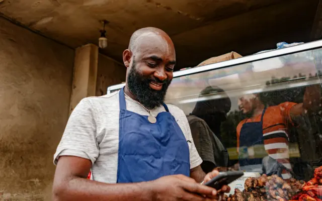 A market trader in an apron checks his smartphone