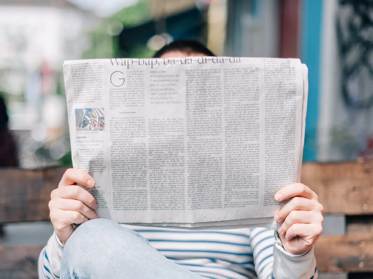 Person reading a newspaper on a wooden bench