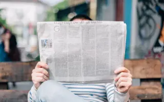 Person reading a newspaper on a wooden bench